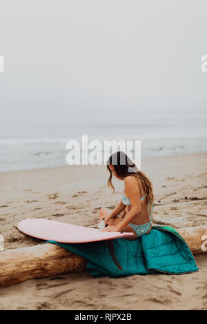 Junge weibliche Surfer sitzen auf log waxing Surfboard am Strand, Ventura, Kalifornien, USA Stockfoto