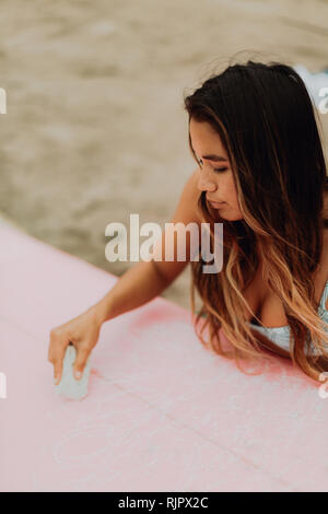 Junge weibliche Surfer waxing Surfboard am Strand, Ventura, Kalifornien, USA Stockfoto
