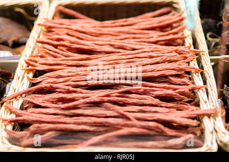 Dünne trockene geräucherte Wurst im Weidenkorb. Kabanossi Wurst. Ansicht von oben Stockfoto