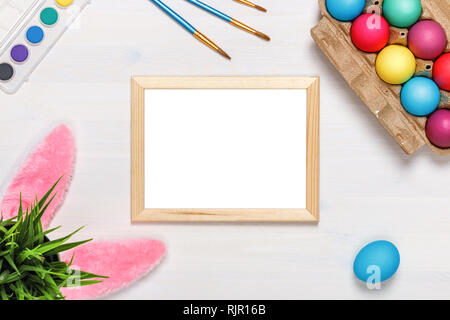 Ein Frame, bunny Ohren, einen Blumentopf mit künstlichem Gras, bunte Eier im Karton, Farben und Pinsel. Ostern Konzept. Platz kopieren Stockfoto