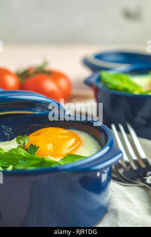 Eier kokot Cocotte französisches Frühstück. Gebackene Eier in blau Keramik Backformen. Portioniert Auflauf aus Gemüse und Eier im italienischen Stil. Nahaufnahme Stockfoto