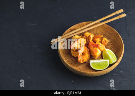 Gebratene Garnelen tempura mit Kalk in Holzplatte auf dunklen Betonoberfläche Hintergrund. Kopieren Sie Text. Tempura Meeresfrüchte Teller serviert japanische oder Stockfoto