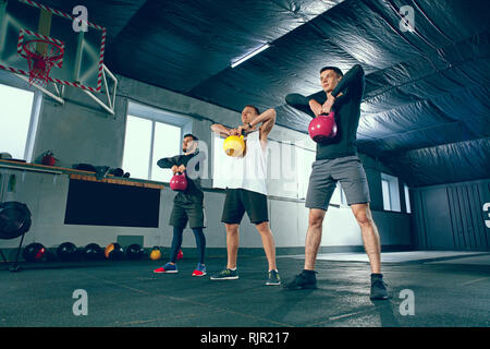 Die konzentrierte und motivierte starke junge Männer in Sportbekleidung Fitness Übungen hockend mit den Kettlebells im Fitnessstudio. Gesunder Lebensstil Konzept Stockfoto