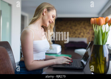 Blonde Frau lachend, während auf Laptop online zu Hause chatten Stockfoto