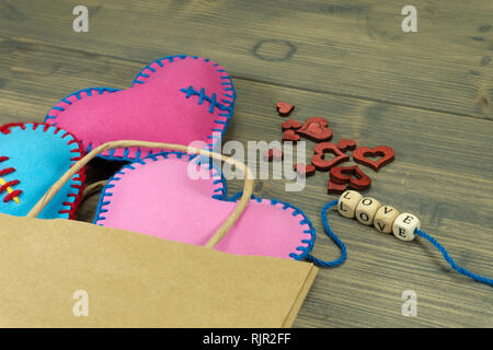 Papiertüte voller Souvenirs und handgefertigten Herz Liebesbriefe auf rustikalen Holzmöbeln Hintergrund. Liebe, Beziehung, Valentinstag, gebrochene Herzen Konzept Stockfoto