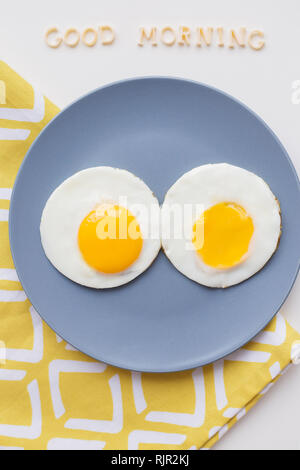 Zwei Eier auf einer Platte und einem gelben Serviette, Beschriftung Guten Morgen Stockfoto