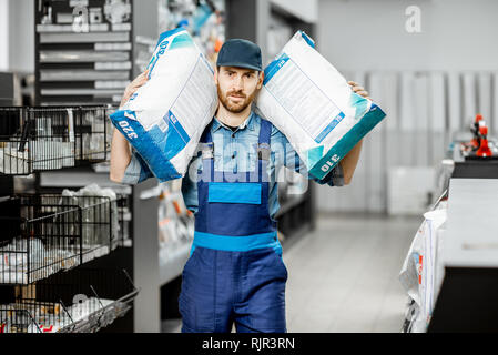 Porträt einer stattlichen Arbeiter im Blaumann holding Taschen mit Bau Mischung im Gebäude Supermarkt Stockfoto