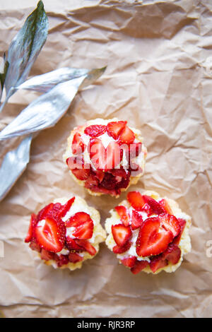 Schöne kleine Kuchen mit Erdbeeren zusammen mit einem Zweig auf Kraftpapier. Stockfoto