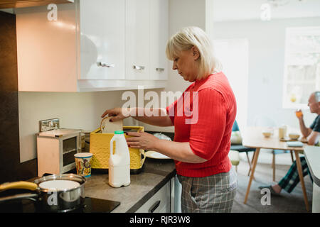 Reife Frau setzt Weißbrotscheiben in einen Toaster zu Hause für Ihr Frühstück. Stockfoto