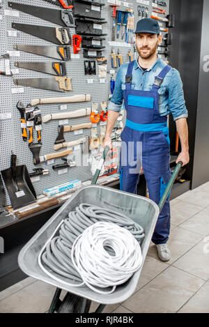 Porträt einer stattlichen Arbeiter in Uniform stehend mit schubkarre in der Nähe der Vitrine mit Garten im Shop Stockfoto