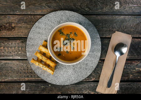 Kürbis creme Suppe in der Keramik Schüssel mit Kürbiskernen und Croutons auf Holz- Hintergrund. Stockfoto
