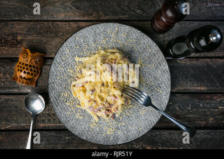 Pasta Carbonara mit Schinken und Parmesan, serviert mit dem Besteck und Pfeffer Mühle auf dem Holz- Hintergrund. Stockfoto