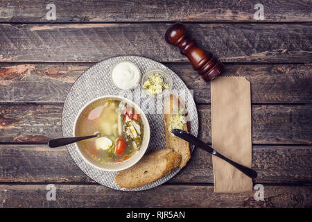 Diät Sauerampfersuppe mit wachtel Eier, Tomaten, Croutons und Sauerrahm. Von Besteck und Pfeffer Mühle auf einen hölzernen Tisch serviert Stockfoto