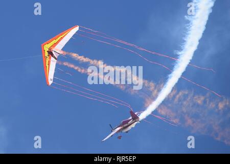 Ein Propeller angetriebene Flugzeug fliegt in der Nähe von Hang Glider, Schneiden der Bänder hinter dem Drachen in eine erstaunliche Leistung, Präzision fliegen Stockfoto