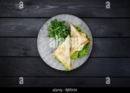 Sandwich mit Hähnchen und Gemüse auf einer Keramikplatte. Auf schwarzem Hintergrund Holz, Ansicht von oben Stockfoto