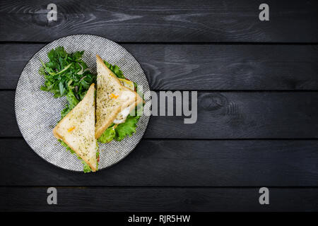 Sandwich mit Hähnchen und Gemüse auf einer Keramikplatte. Auf schwarzem Holz- Hintergrund. Ansicht von oben, kopieren Sie Platz für Ihren Text Stockfoto