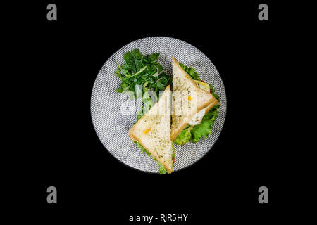 Sandwich mit Hähnchen und Gemüse auf einer Keramikplatte. Auf dem schwarzen Hintergrund isoliert, Ansicht von oben Stockfoto