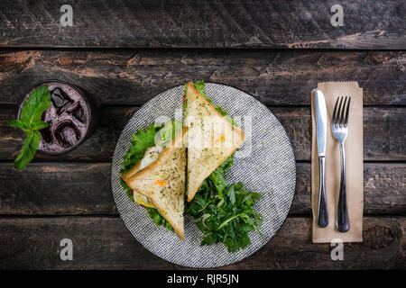 Sandwich mit Hähnchen und Gemüse auf einer Keramikplatte. Mit Besteck und frische Limonade serviert. Ansicht von oben Stockfoto