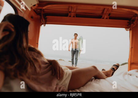 Junge Frau Liegesitze in der Rückseite der recreational vehicle Warten auf Surfer Freund am Strand, Jalama, Ventura, Kalifornien, USA Stockfoto