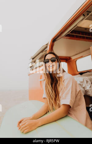 Junge weibliche Surfer auf recreational vehicle am Strand, Jalama, Ventura, Kalifornien, USA sitzen Stockfoto
