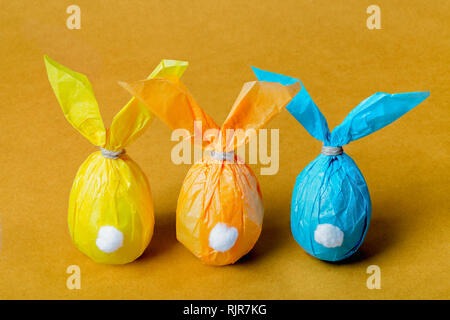 Drei bunte Ostereier in Form von Ostern Kaninchen auf einem hellen orange Hintergrund Stockfoto