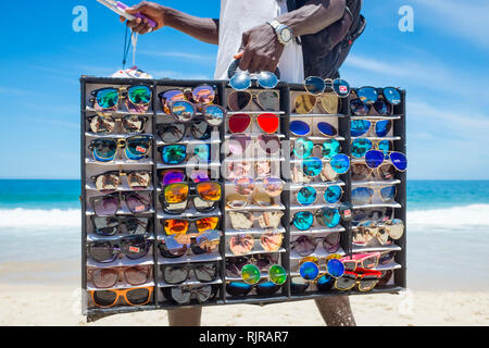 RIO DE JANEIRO - Januar, 2017: Eine afrikanische Einwanderer Verkauf gefälschter Sonnenbrille geht mit einer Vitrine auf der Suche nach Kunden am Strand von Ipanema. Stockfoto