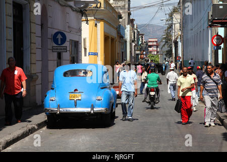 SANTIAGO DE KUBA - 10. Februar: Menschen gehen vorbei an alten Autos am 10. Februar 2011 in Santiago de Cuba. Gesetz Änderung können die Kubaner Autos wieder Handel Stockfoto