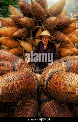 Alte Vietnamesische männlichen Handwerker mit Fahrrad, die die traditionellen Bambus Fish trap oder Weben an der alten traditionellen Haus in Do sy Vill Stockfoto