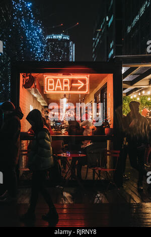 London, Großbritannien - 26 Januar, 2019: Menschen vorbei gehen. beleuchtete Fenster und Leuchtreklame auf Bar in Canary Wharf an einem regnerischen Abend. Canary Wharf ist ein Beschäftigter Stockfoto