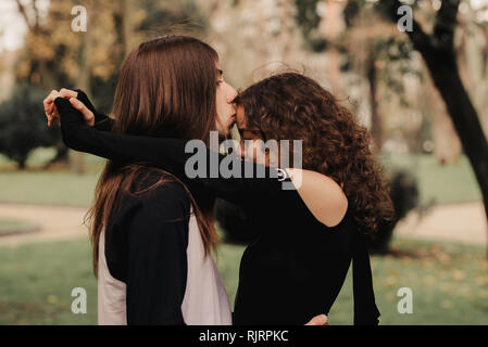 Langhaariger Mann umarmt und küsst Frau in der Nähe von Baum Stockfoto