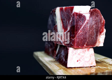 Große Stücke von streaky Rindfleisch für Roh Fütterung von Katzen und Hunden auf Holzbrett vor dunklem Hintergrund Stockfoto