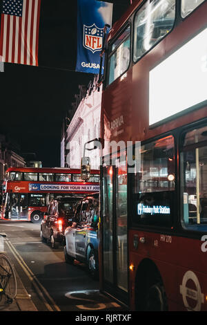 London, Großbritannien - 17 Dezember, 2018: Die schwarzen Taxis und Busse an der Regent Street, London, in der Nacht. Die Straße ist dekoriert mit NFL Flaggen die auch zu feiern. Stockfoto