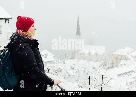 Frau in Red Hat genießt die Aussicht über Hallstatt Altstadt während der Schneesturm, Österreich. Stockfoto