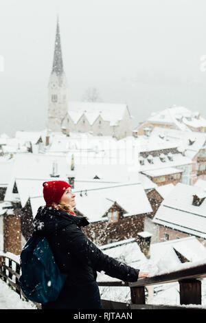 Frau in Red Hat genießt die Aussicht über Hallstatt Altstadt während der Schneesturm, Österreich. Vertikale Ausrichtung. Stockfoto