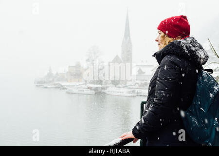 Frau in Red Hat genießt die Aussicht über Hallstatt Altstadt während der Schneesturm, Österreich. Stockfoto
