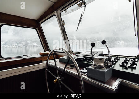 HALLSTATT, Österreich - Januar 2019: Blick über Hallstatt Stadt und Alpen von der Fähre Kapitänskajüte. Lenkrad im Vordergrund. Stockfoto