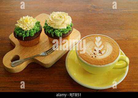 Kaffeepause mit einer Tasse heißen Cappuccino und zwei Cupcakes gekrönt mit Blume geformte Schlagsahne Stockfoto