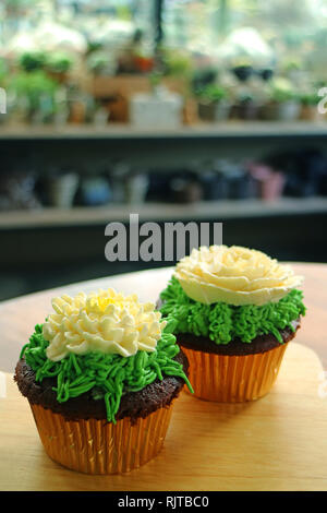 Zwei cupcakes gekrönt mit Blume geformte Creme auf Holztisch mit verschwommenen Zimmer im Hintergrund Schlagsahne serviert. Stockfoto