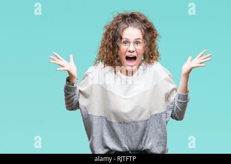 Schöne Brünette lockige Haare junge Mädchen Tragen einer Brille über isolierte Hintergrund verrückt und erstaunt, Feiern für den Erfolg mit erhobenen Armen und offene e Stockfoto