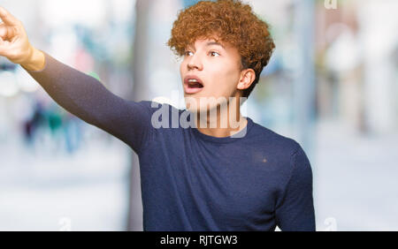 Junger stattlicher Mann mit afro Haar zeigte mit dem Finger vor überrascht, offenem Mund erstaunt Ausdruck, etwas vor Stockfoto