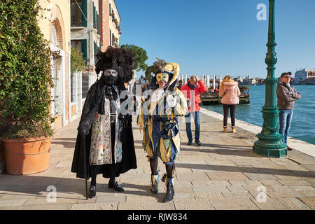 Venedig, Italien - Februar 10, 2018: Zwei Männer in Masken und Schwarz bauta und jester Kostüme auf der Grand Canal Street während des Karnevals Stockfoto