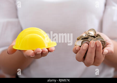 Nahaufnahme einer Hand, die eine Gelbe einer Person hardhat und goldenen Münzen Stockfoto