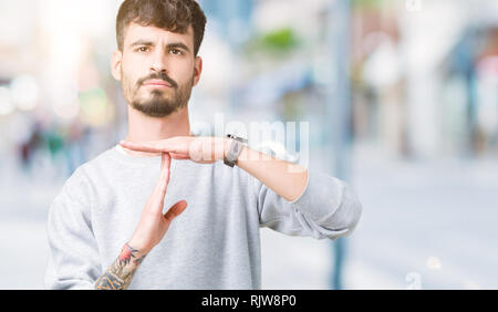 Jungen gutaussehenden Mann mit Sweatshirt über isolierte Hintergrund tun time out Geste mit den Händen, frustriert und ernstes Gesicht Stockfoto