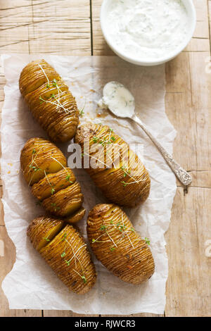 Hasselback Kartoffeln mit Käse und saurer Sahne Soße auf einer hölzernen Tisch. Im rustikalen Stil. Stockfoto