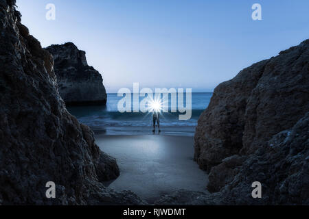 Mann, beleuchtete Scheinwerfer, stehend am Strand von Waters Edge bei Sonnenuntergang, Alvor, Algarve, Portugal, Europa Stockfoto