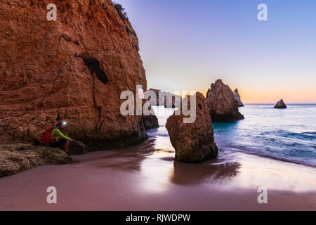 Mann sitzt von Cliff mit beleuchteten Scheinwerfer, Alvor, Algarve, Portugal, Europa Stockfoto