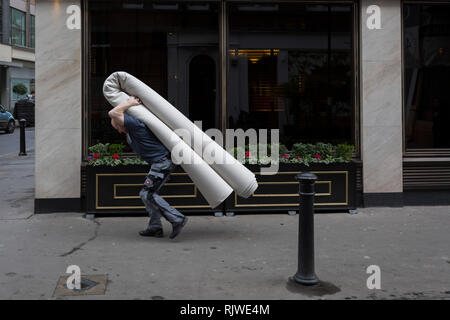 Ein Mann trägt eine schwere neu aufgerollten Teppich auf seinem Rücken ein West End Hotel, am 6. Februar 2019 in London, England. Stockfoto