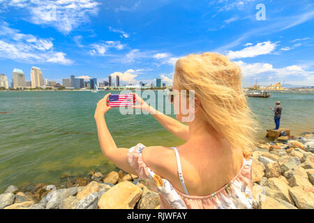 Blond touristische nimmt Foto von San Diego von Skyline per Handy mit amerikanischer Flagge. Weibliche Lebensstil nimmt Bilder in Kalifornien Sommer Stockfoto