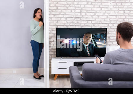 Junge Frau schrie hinter der Mauer mit dem nächsten Mann vor dem Fernseher zu Hause Laut Stockfoto