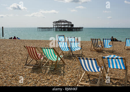 Liegestühle am Strand mit alten West Pier im Hintergrund. Hove, Brighton, East Sussex, England Stockfoto